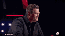 a man in a black shirt is sitting at a table with a nbc logo in the corner