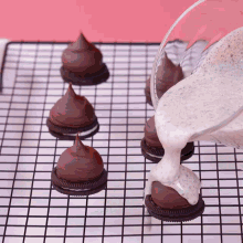 a person pouring frosting on oreos on a wire rack