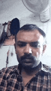 a man in a plaid shirt is standing in front of a white fan