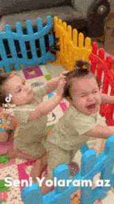 two babies are playing with a toy fence and the caption says seni yolaram az