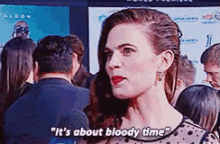 a woman is standing in front of a crowd of people and says it 's about bloody time .