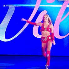 a woman in a pink and red outfit is walking on a stage in front of a blue background .