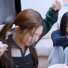 two girls are sitting on a couch and one of them is getting her hair braided