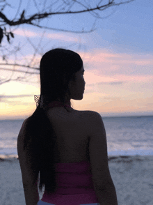 a woman in a pink top stands on the beach looking at the ocean