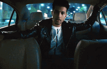 a man in a leather jacket is sitting in the back seat of a car with his arms outstretched