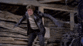 a man in a black leather jacket is standing in front of a pile of wood ..