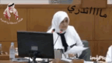 a woman in a hijab is sitting in front of a microphone in front of a computer .