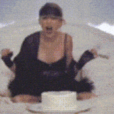 a woman in a black dress is sitting on a bed with a cake in front of her