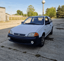 a white suzuki car is parked on a concrete surface