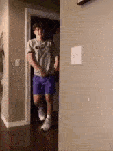 a young man is standing in a hallway wearing shorts and a gray shirt .