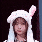 a young girl wearing a white bunny hat with pink ears is making a funny face .