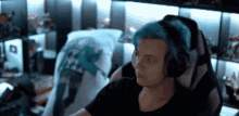 a man with blue hair is wearing headphones while sitting in a chair .