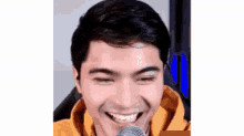 a man in a yellow hoodie is smiling and looking at the camera while sitting in front of a microphone .