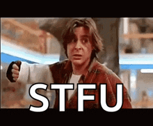 a man in a plaid shirt is pointing at the camera with the word stfu behind him