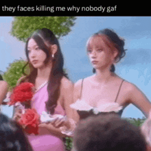 two women in pink dresses are standing next to each other holding roses and talking to each other .