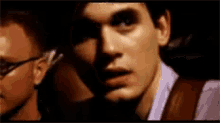 a close up of a man 's face in a dark room with another man behind him .