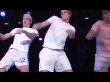a group of men are dancing on a stage and one of them has the number 12 on his shorts
