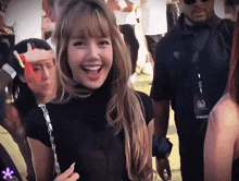 a woman in a black turtleneck smiles while a man in a black shirt stands behind her