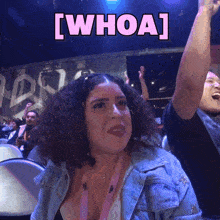 a woman with curly hair is sitting in front of a sign that says " whoa "