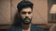 a man with a beard is leaning against a wall in a room .