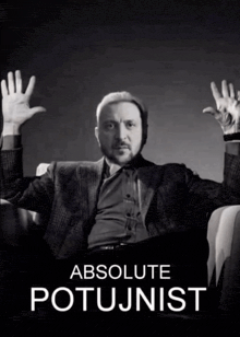 a man in a suit sits in a chair with his hands in the air and the words absolute potujnist behind him
