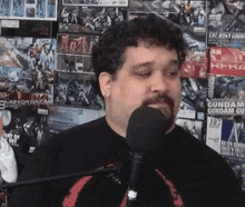a man with a beard is talking into a microphone while standing in front of a wall full of toys .