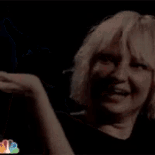 a woman with blonde hair is clapping her hands and smiling .