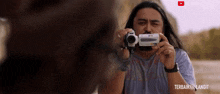 a man with long hair is holding a camcorder in his hands and a youtube logo is visible in the background