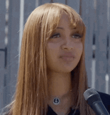 a woman speaking into a microphone wearing a necklace with a circle on it