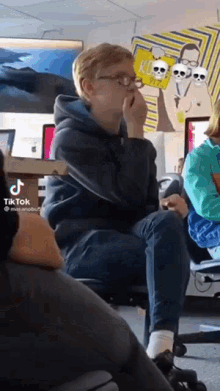 a boy wearing glasses is sitting on a chair in a classroom .