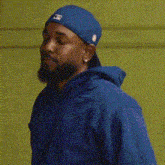 a man wearing a blue hat and a blue hoodie is standing in front of a wall .