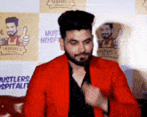 a man in a red jacket is standing in front of a wall that says thakare 's hustlers hospitality