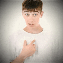 a young man in a white shirt is pointing to his chest