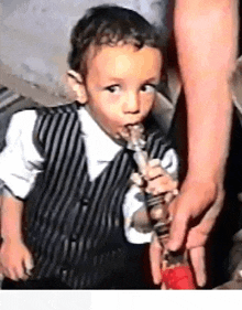a little boy is smoking a hookah while wearing a striped vest .
