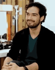 a man with a beard is sitting at a table with his hands folded and smiling at the camera .