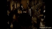 a group of people in tuxedos are standing around a woman in a red dress .