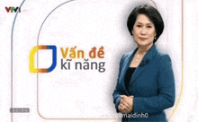a woman in a blue suit is standing in front of a sign that says ' van de ki nang ' on it .