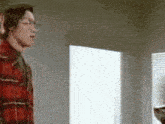 a man in a plaid shirt is standing in front of a white wall
