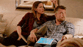 a man and a woman sitting on a couch with a tablet
