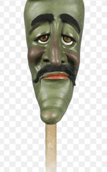 a green puppet head with a mustache is on a stick