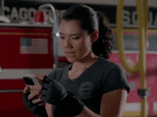 a woman wearing black gloves is looking at her cell phone .