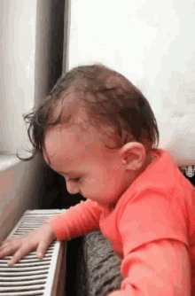 a baby in a red shirt is crawling over a radiator .