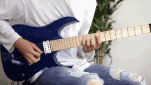 a man is playing a blue electric guitar while sitting on a chair .