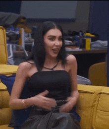 a woman in a black top is sitting on a yellow couch smiling