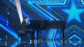 a man in a suit is playing a piano on a stage with a star background