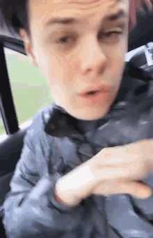 a young man is sitting in the back seat of a car with his eyes closed and his mouth open .