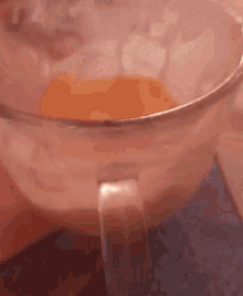 a close up of a glass bowl with a handle filled with orange liquid .