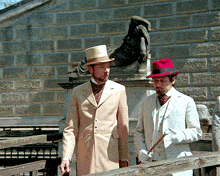 a man in a top hat stands next to another man in a white suit and white gloves