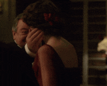 a man in a tuxedo is touching the back of a woman 's head