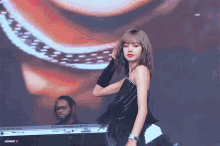 a woman in a black dress is dancing on a stage with a man playing a keyboard in the background .
